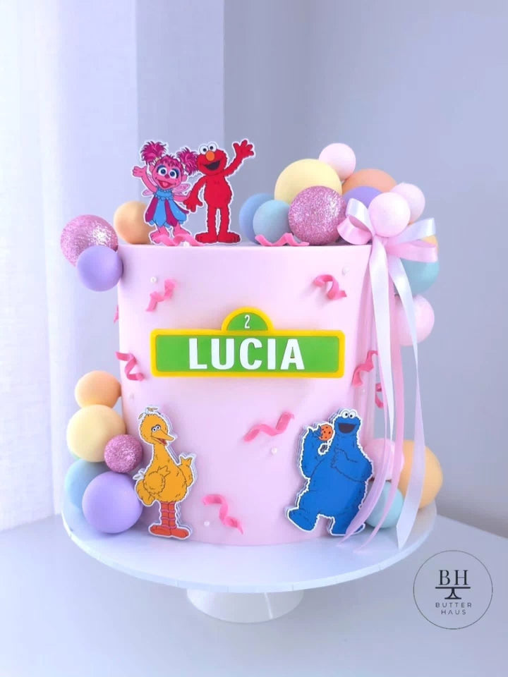 Pale pink birthday cake with Sesame Street inspired character toppers and pastel spheres