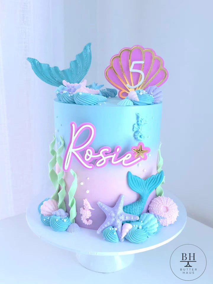 Blue to pink ombre mermaid cake with mermaid tail, seashell age topper and sea details
