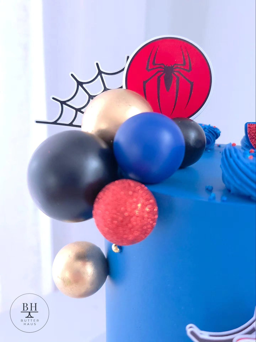 Side view of Spiderman birthday cake with spiderweb toppers and red and blue ball cluster