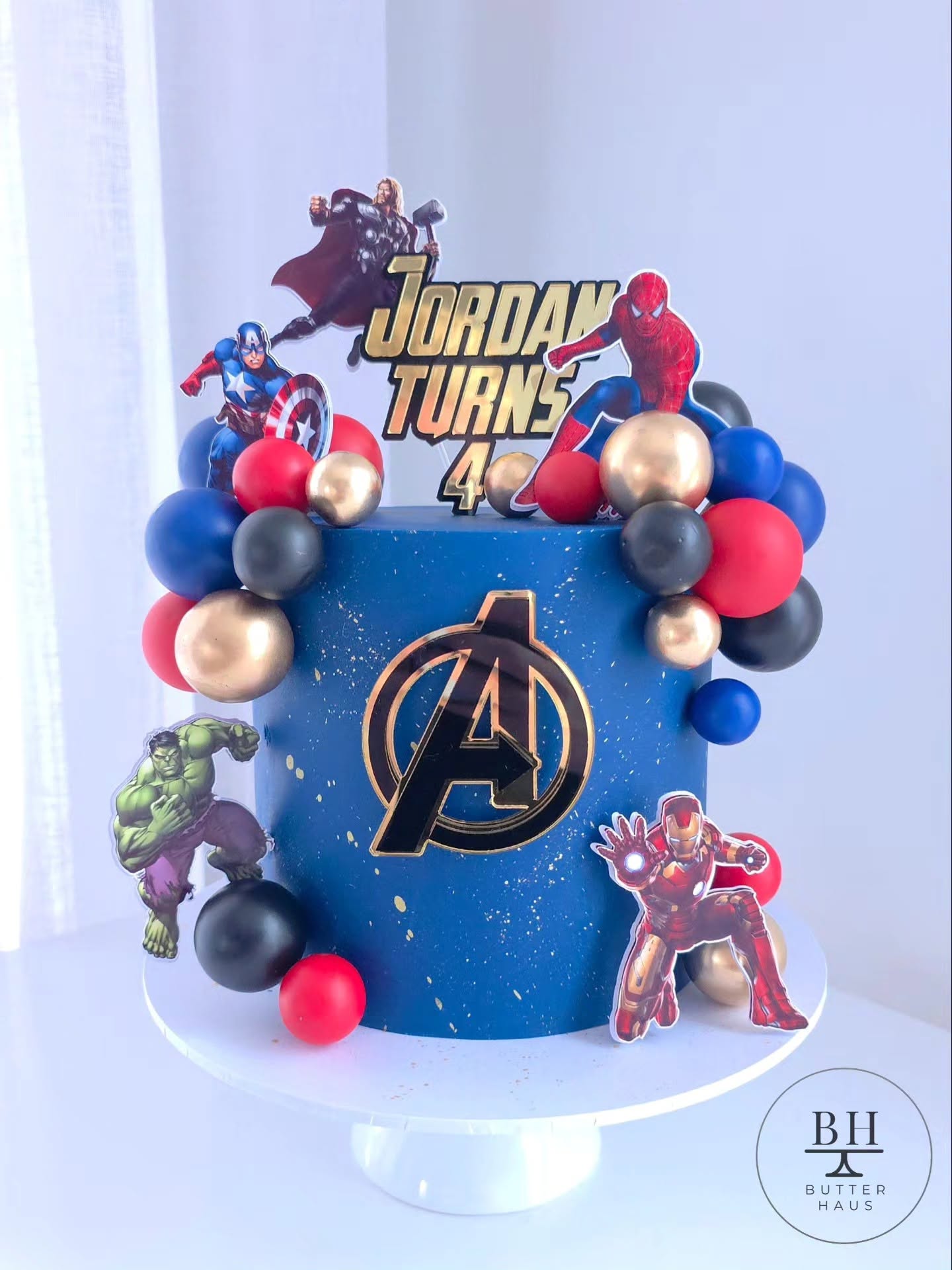 Close-up of gold-speckled galaxy-effect Avengers birthday cake with Iron Man cardstock cutout and navy, red and rose gold balloon cluster