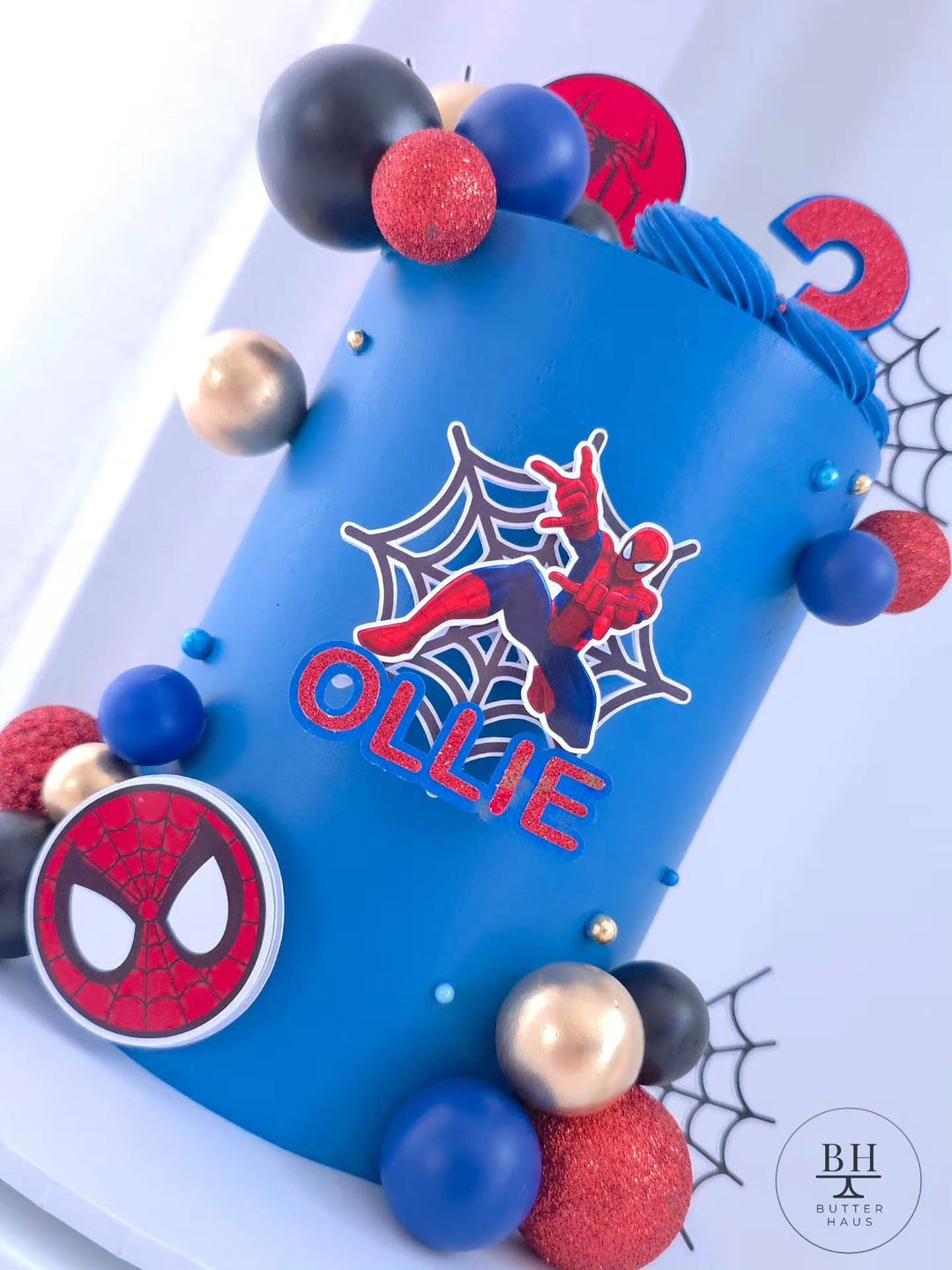 Spiderman birthday cake with custom name topper and Spiderman mask detail on blue buttercream
