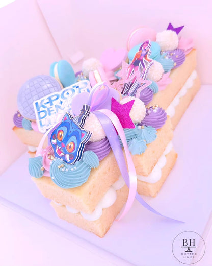 Close-up of the K-pop demon hunter number cake showing macarons, chocolates and the double-layered bow detail