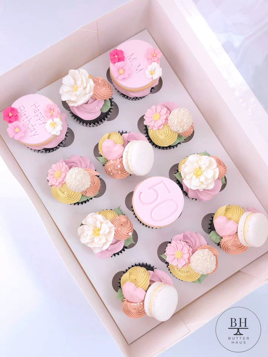 Box of pink, peach and yellow cupcakes with piped buttercream flowers and macarons