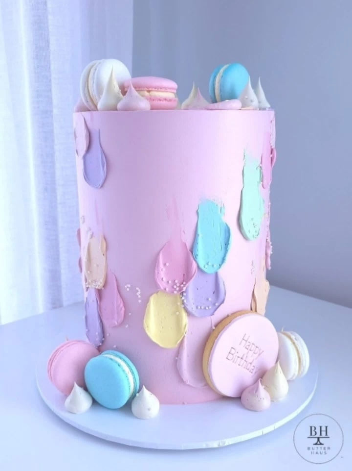 Pink birthday cake with pastel brushstrokes, macarons, meringue kisses and Happy Birthday plaque