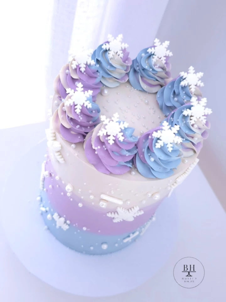 White to lilac and blue birthday cake with swirled rosettes and white fondant snowflakes