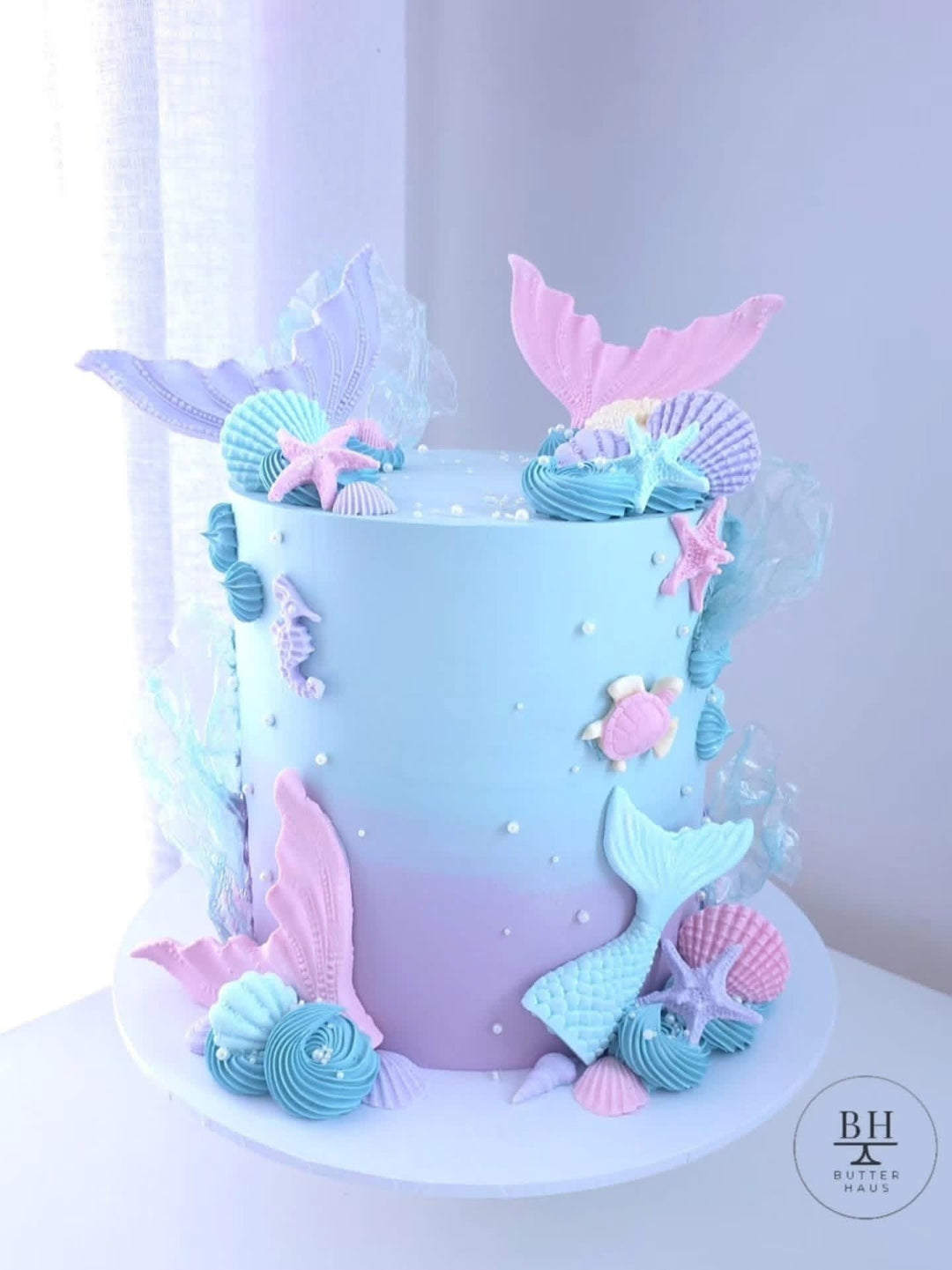 Pale blue and lilac birthday cake with pastel mermaid tails, seashells and starfish