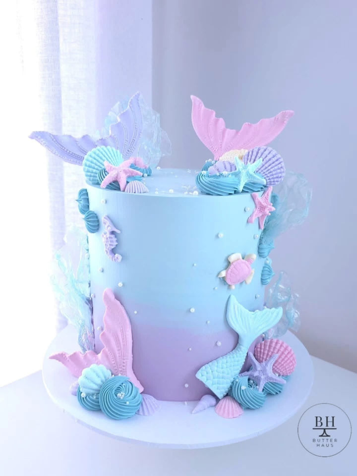 Pale blue and lilac birthday cake with pastel mermaid tails, seashells and starfish