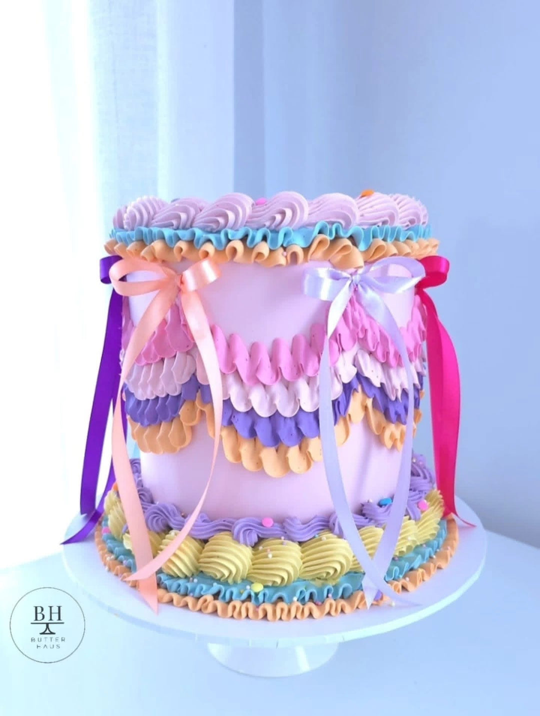 Pale pink vintage birthday cake with multicoloured piped ruffles, swags and long satin ribbon bows