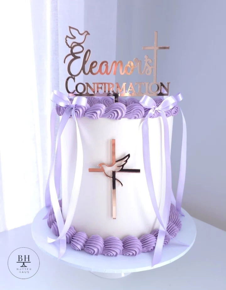 White buttercream cake with lilac rosettes, lilac satin bows, rose-gold cross, dove and name topper