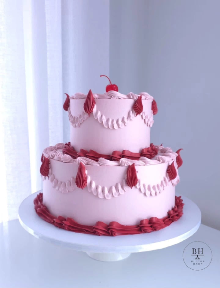 Two tier pale pink vintage cake with red ruffles, pink swags and a cherry