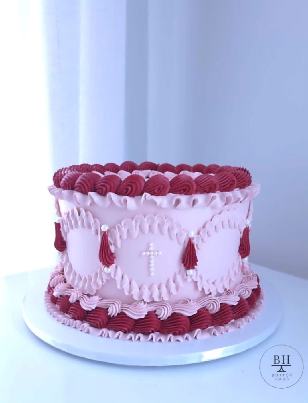Pale pink vintage cake with red and pink piped swags and a white pearl cross