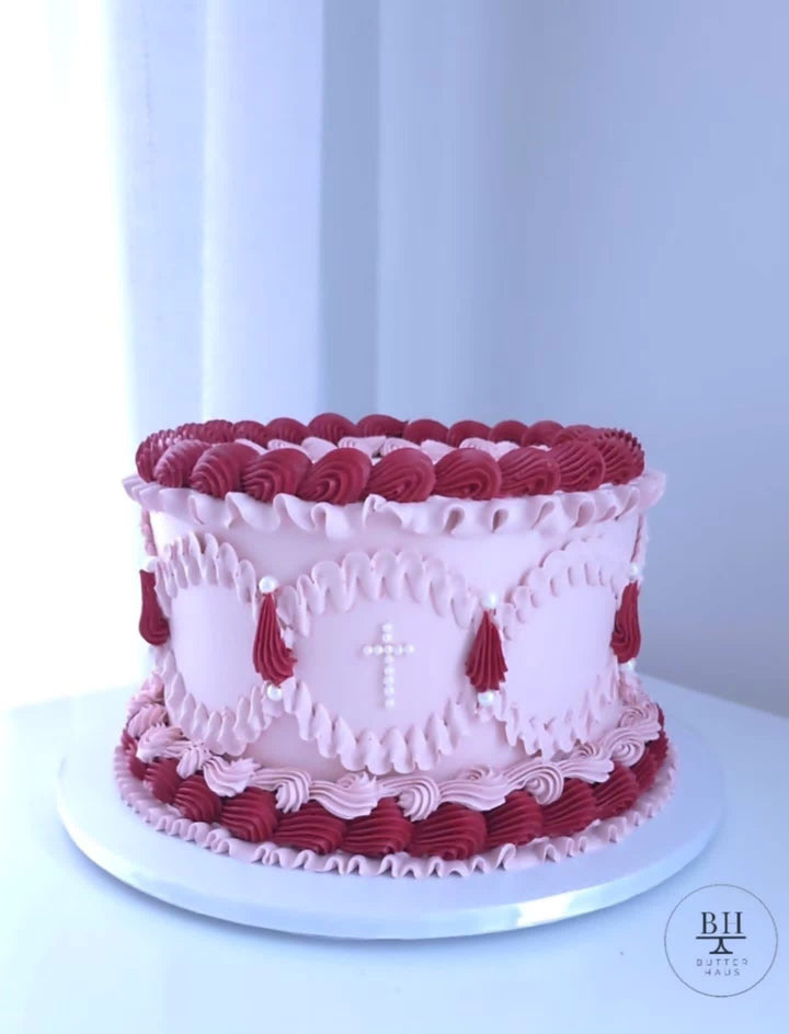 Pale pink vintage cake with red and pink piped swags and a white pearl cross