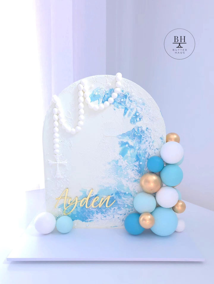 Upright white arch cake with blue brush strokes, a pearl rosary with cross and gold spheres