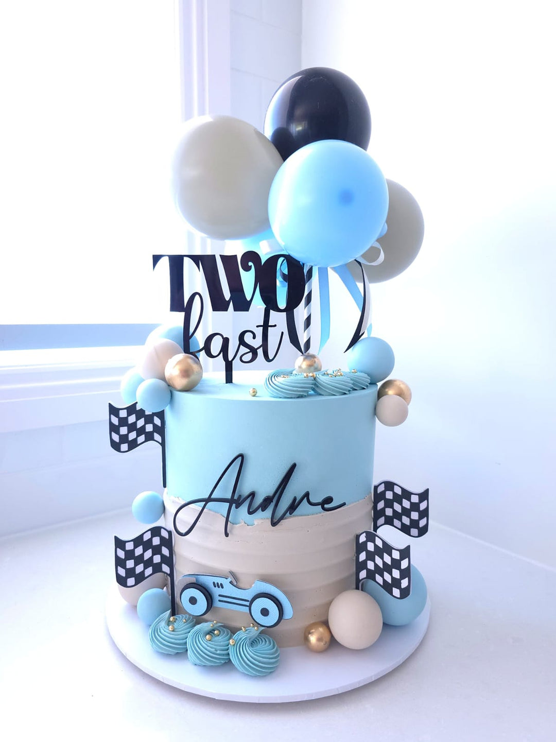 The Victory Lap birthday cake with blue and sand buttercream, race car cutout and balloon garland