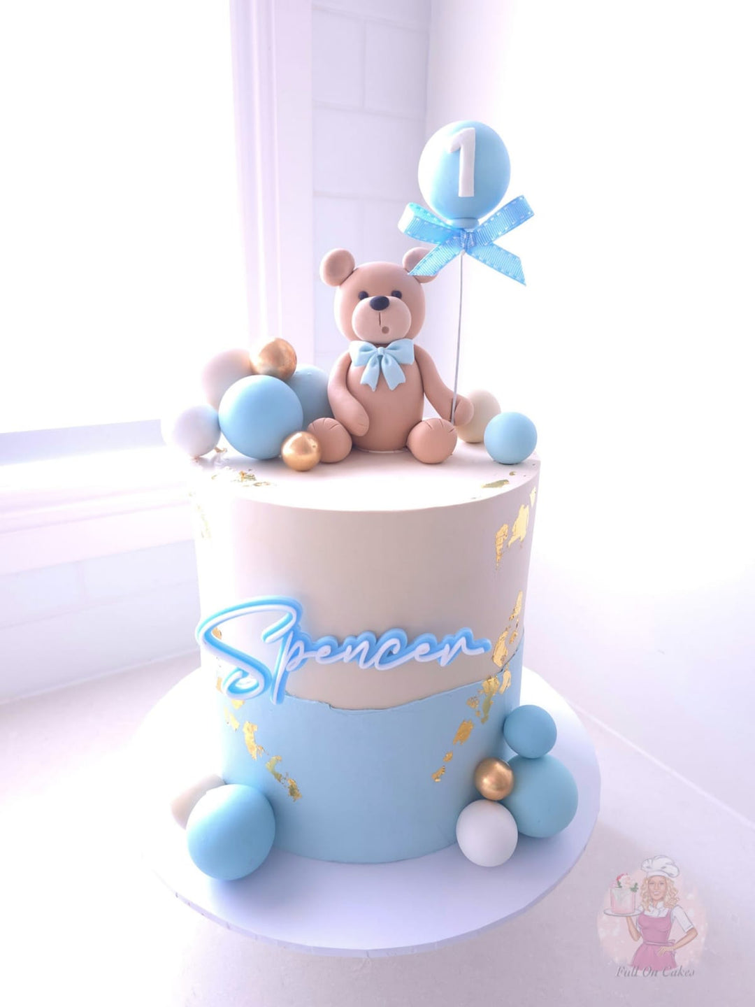 Cream and pale blue teddy bear birthday cake with gold leaf and balloon age topper