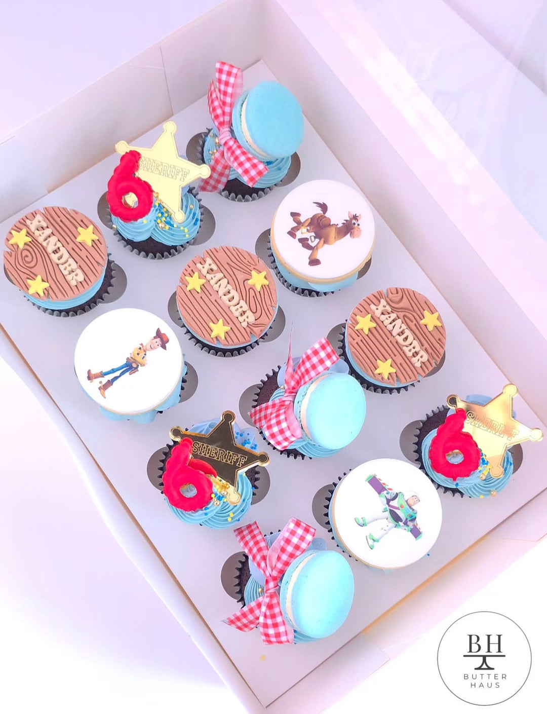 Box of blue cupcakes with Toy Story inspired character discs, sheriff stars and macarons