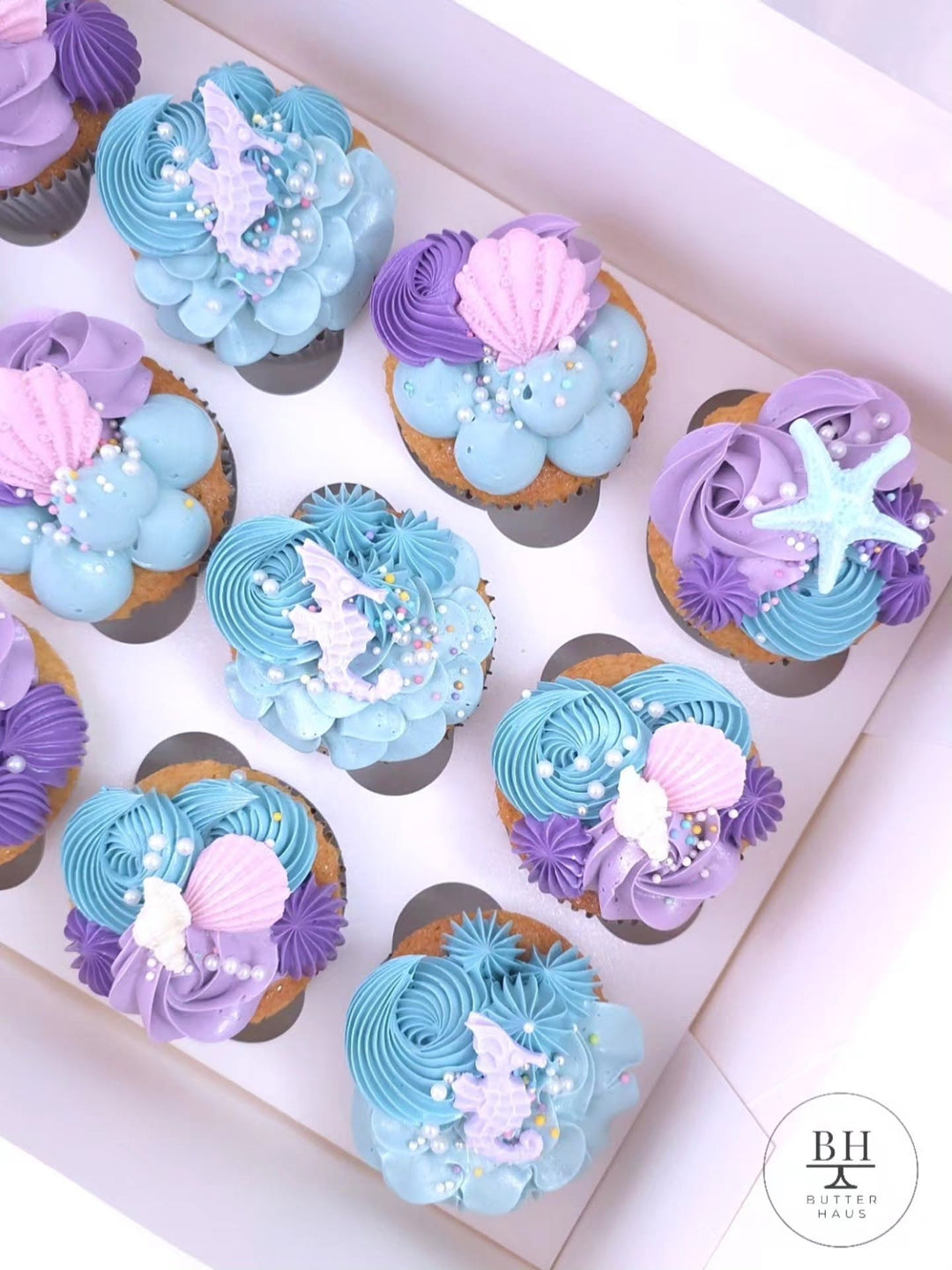 Box of teal and purple cupcakes with pink seashells, starfish and lilac mermaid tails