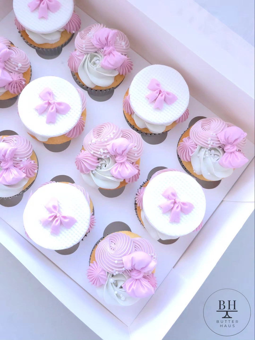 Box of pink and white cupcakes with quilted fondant discs and pink fondant bows