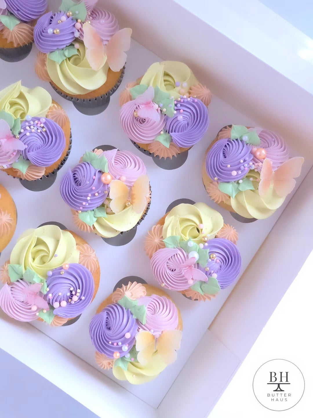Box of purple, yellow and pink rosette cupcakes with edible butterflies and pearls