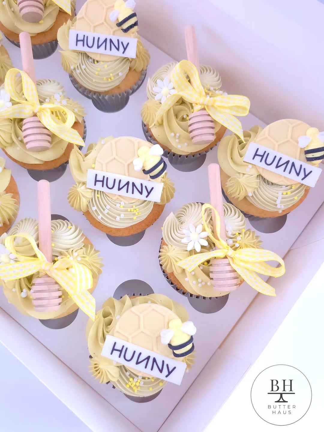 Box of pale yellow cupcakes with honeycomb HUNNY discs, fondant bees and honey dippers