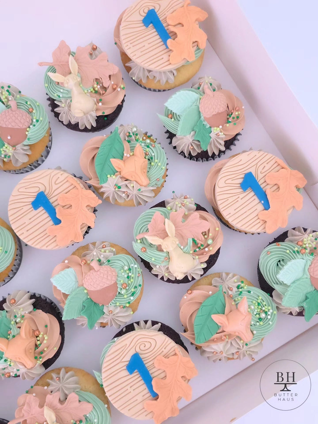 Box of sage green and peach cupcakes with fondant foxes, bunnies, acorns and leaves